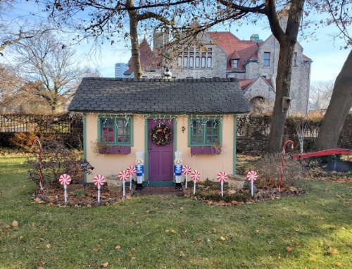 A whimsical holiday-themed miniature house with candy cane decorations and a wreath, set in a grassy yard.