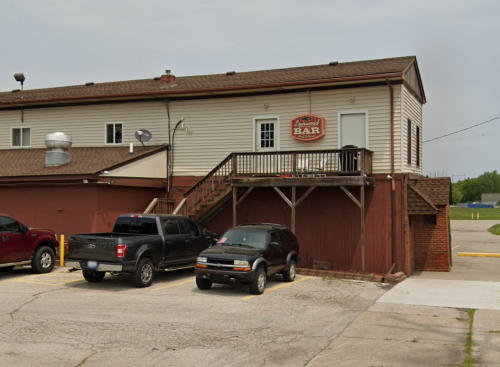 A two-story building with a sign reading "Bar," featuring a staircase and parked vehicles in the foreground.