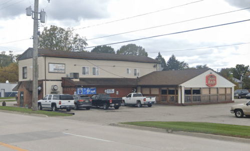 A two-story building with a bar sign, surrounded by parked trucks and cars, on a cloudy day.