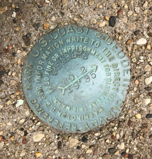 A circular metal survey marker embedded in gravel, inscribed with "US Coast and Geodetic Survey 1935."