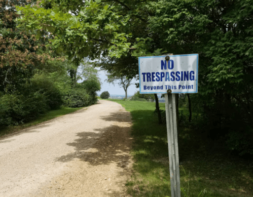 A dirt road lined with trees, featuring a sign that reads "No Trespassing Beyond This Point."