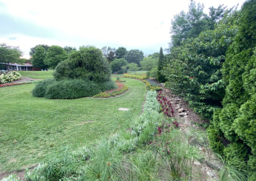 A lush garden with winding paths, colorful flower beds, and greenery under a cloudy sky.