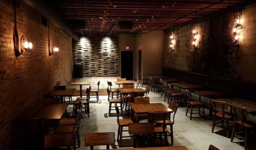 A dimly lit restaurant interior featuring wooden tables and chairs, exposed brick walls, and decorative lighting.