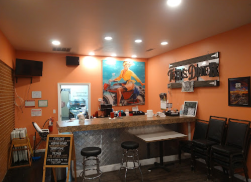 A cozy diner interior with orange walls, a counter, bar stools, and a vintage mural of a woman on a car.