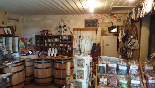 A cozy shop interior featuring wooden barrels, shelves of goods, and a chalkboard menu.