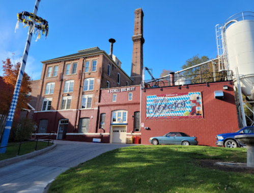 Historic brewery building with a tall chimney, colorful signage, and a clear blue sky in the background.