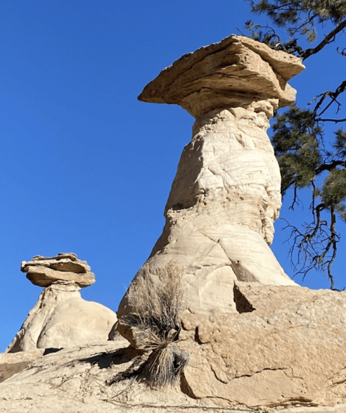 Two unique rock formations stand against a clear blue sky, resembling natural sculptures in a desert landscape.