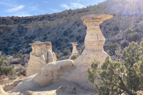 Unique rock formations rise against a blue sky, surrounded by rugged terrain and sparse vegetation.