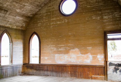 Interior of an abandoned building with wooden walls, arched windows, and a circular window above.