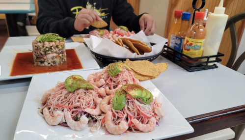 A plate of shrimp pasta with avocado, a seafood tower, and tortilla chips on a table with sauces in the background.