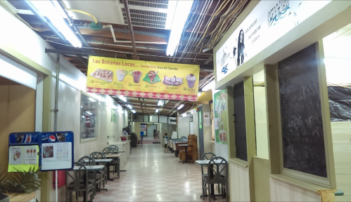 A hallway in a food court with tables, chairs, and colorful banners advertising snacks and desserts.