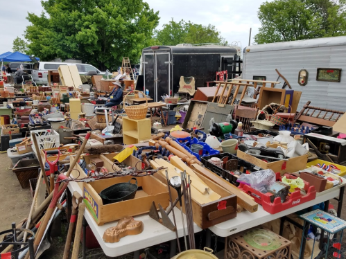 A cluttered outdoor market stall filled with various antiques, tools, and household items.