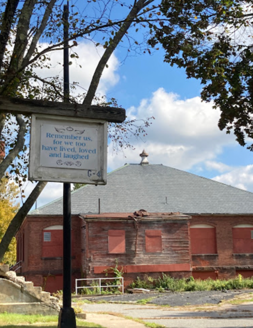 A weathered sign in front of an old building with a quote about living, loving, and laughing under a blue sky.