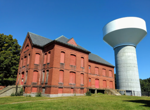 A red brick building next to a tall, cylindrical water tower against a clear blue sky.