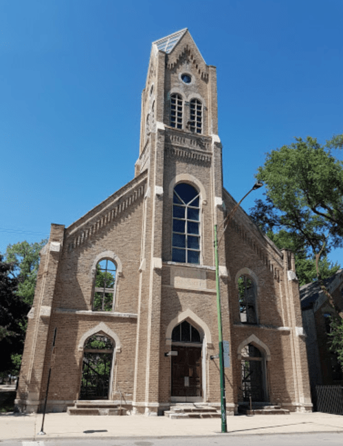 Historic brick church with a tall tower, large windows, and a clear blue sky in the background.