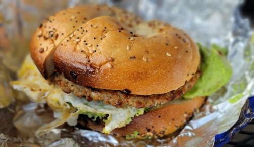 A toasted sesame bagel sandwich with a sausage patty, fried egg, and lettuce, wrapped in foil.