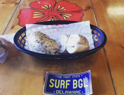 A basket with two rolls on a paper napkin, placed on a wooden table with a hibiscus design and a sticker from Delaware.