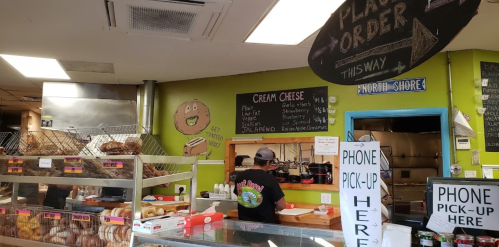 A bakery counter with a menu board, displaying cream cheese options, and a staff member preparing orders.