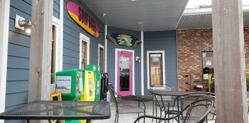 Exterior view of a colorful café with outdoor seating and a vibrant entrance, featuring newspaper stands.