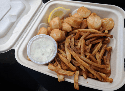 A takeout container filled with golden fries, breaded fish pieces, and a lemon wedge, accompanied by a small cup of tartar sauce.
