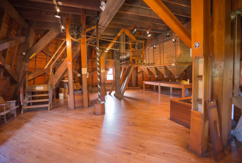 Interior of a wooden building with exposed beams, large open space, and various structures for storage or display.