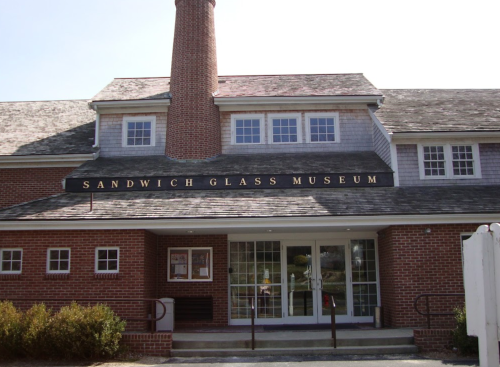 Exterior of the Sandwich Glass Museum, featuring a brick facade and a prominent sign above the entrance.