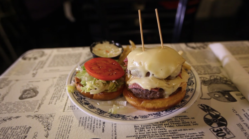 A juicy burger with melted cheese, lettuce, and tomato, served with fries on a patterned table.