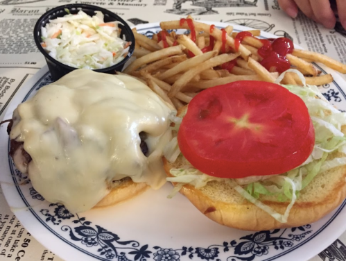 A plate with a cheeseburger topped with melted cheese, lettuce, and tomato, served with fries and coleslaw.
