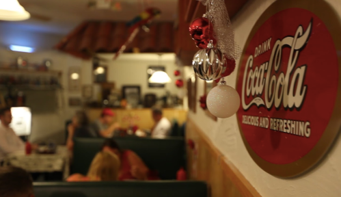 A cozy diner scene with a vintage Coca-Cola sign and festive decorations, featuring patrons enjoying their meals.