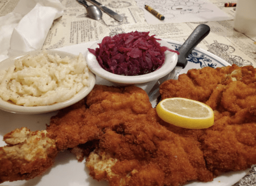 A plate featuring a large fried chicken cutlet, mashed potatoes, and a side of red cabbage, garnished with a lemon slice.