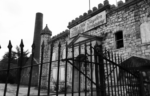 Black and white image of the Old Taylor Distillery, featuring a stone building and a wrought iron fence.