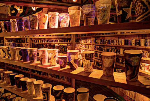 A display of colorful, hand-painted cups arranged on wooden shelves, illuminated by warm lighting.