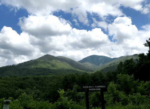 Scenic view of green mountains under a cloudy sky, with a sign for Carlos C. Campbell Overlook in the foreground.