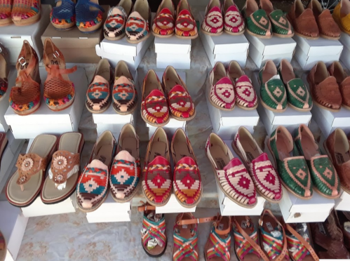 A variety of colorful, handcrafted shoes displayed on white boxes at a market.