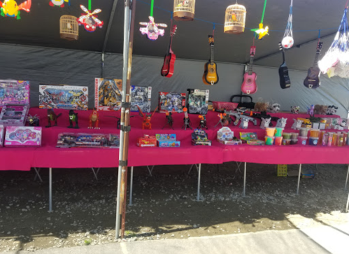 A colorful market stall with toys, games, and crafts displayed on pink tables under a tent.