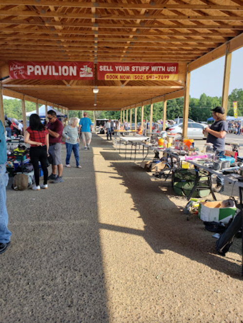 A bustling outdoor market with vendors and shoppers under a wooden pavilion, showcasing various items for sale.