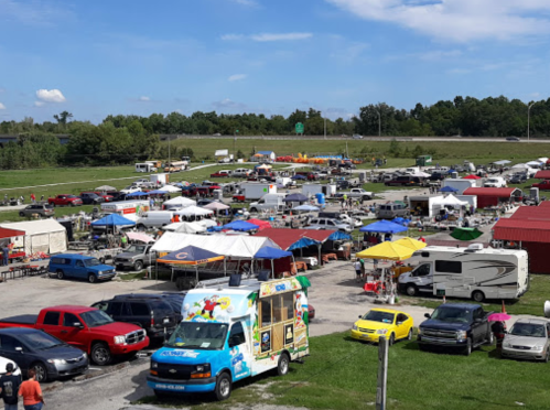 Aerial view of a bustling outdoor market with colorful tents, food trucks, and numerous vehicles parked nearby.