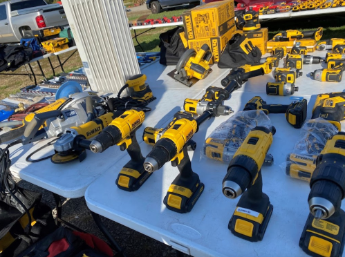 A table displaying various yellow and black power tools, including drills and saws, at an outdoor market.