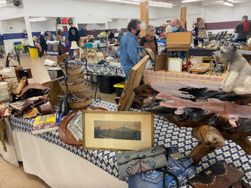 A bustling indoor market with various vintage items, crafts, and people browsing among tables filled with goods.