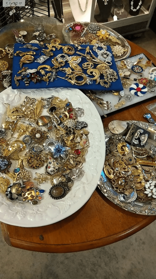 A collection of vintage brooches and jewelry displayed on plates and trays, featuring various designs and colors.