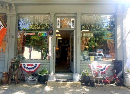 A charming antique shop with large windows, patriotic decorations, and a welcoming entrance.