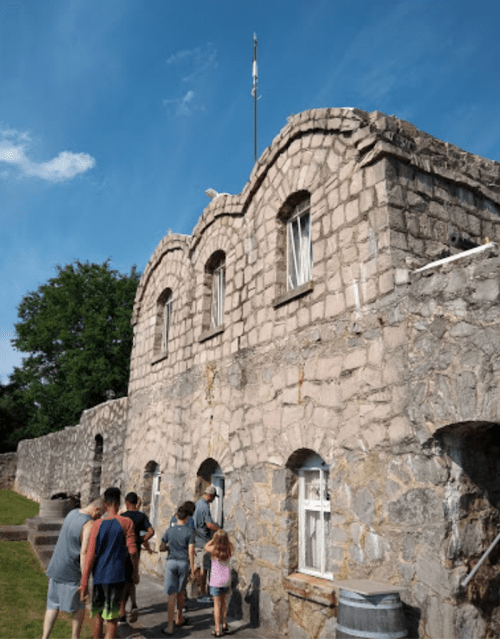 A group of people walks towards a stone building with arched windows under a blue sky.