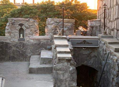 Stone structure with steps leading to a dark entrance, surrounded by trees and bathed in warm sunset light.