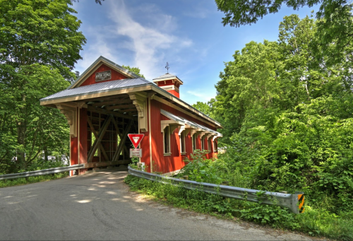 A red covered bridge surrounded by lush green trees under a clear blue sky.