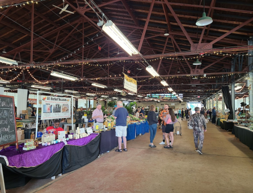 A bustling market scene with vendors selling goods, colorful displays, and visitors browsing under string lights.