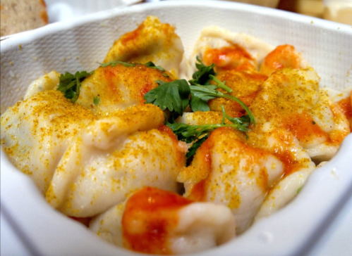 A close-up of dumplings topped with sauce and sprinkled with spices, garnished with fresh cilantro in a white container.