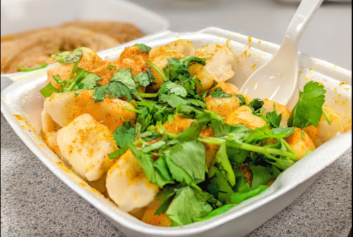 A takeout container filled with dumplings topped with cilantro and spices, served with a plastic spoon.