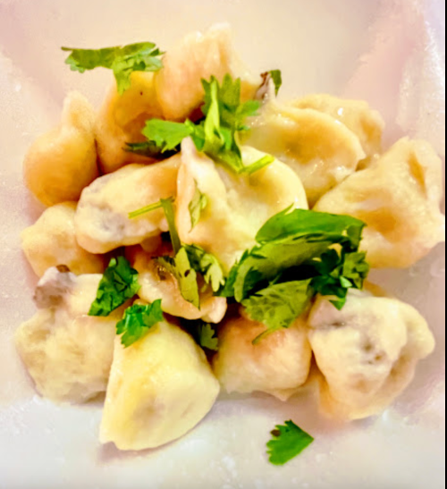 A bowl of dumplings topped with fresh cilantro, served in a light sauce.