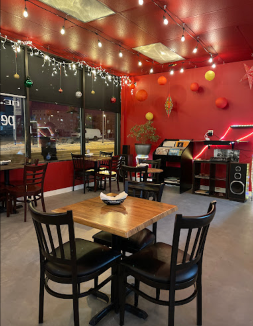 Cozy restaurant interior with red walls, string lights, and wooden tables, featuring a record player and festive decorations.