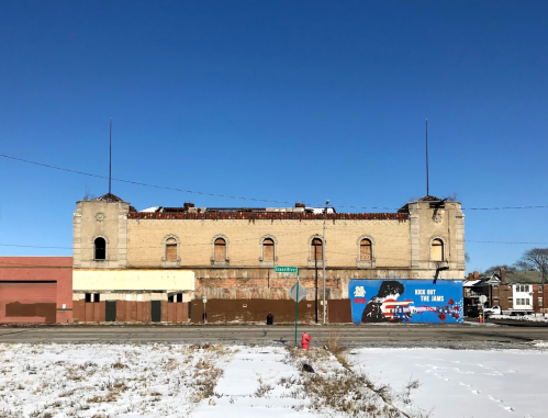 Abandoned building with a damaged roof, blue sky, and a colorful mural on the adjacent wall, surrounded by snow.